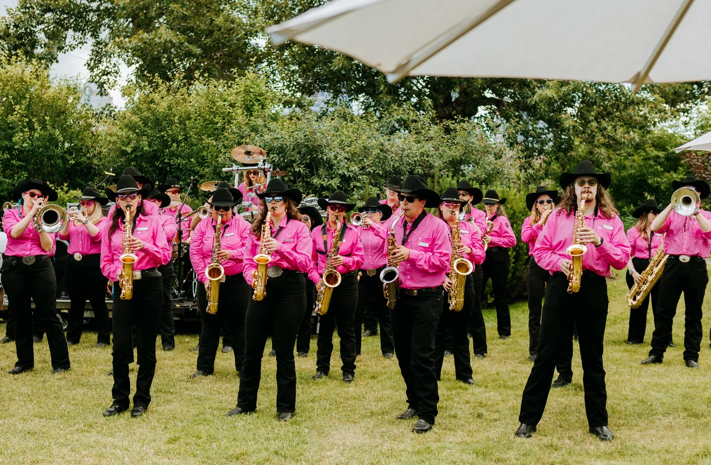 The Band of Outriders in pink shirts and black cowboy hats, playing brass on the lawn at Ace High 2026.